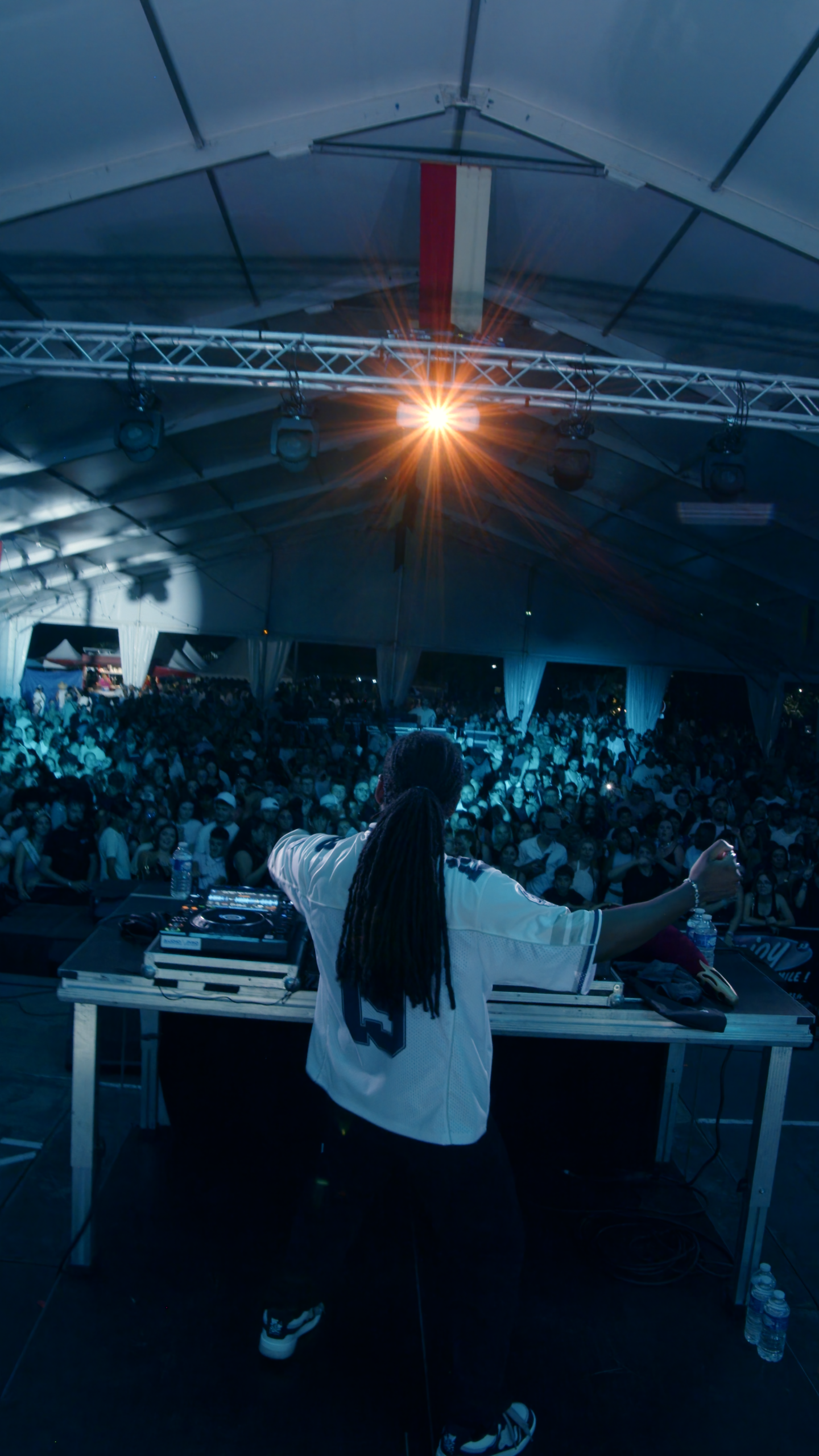 Un vidéaste à Bordeaux capture un DJ en performance devant une foule enthousiaste sous un chapiteau lumineux.